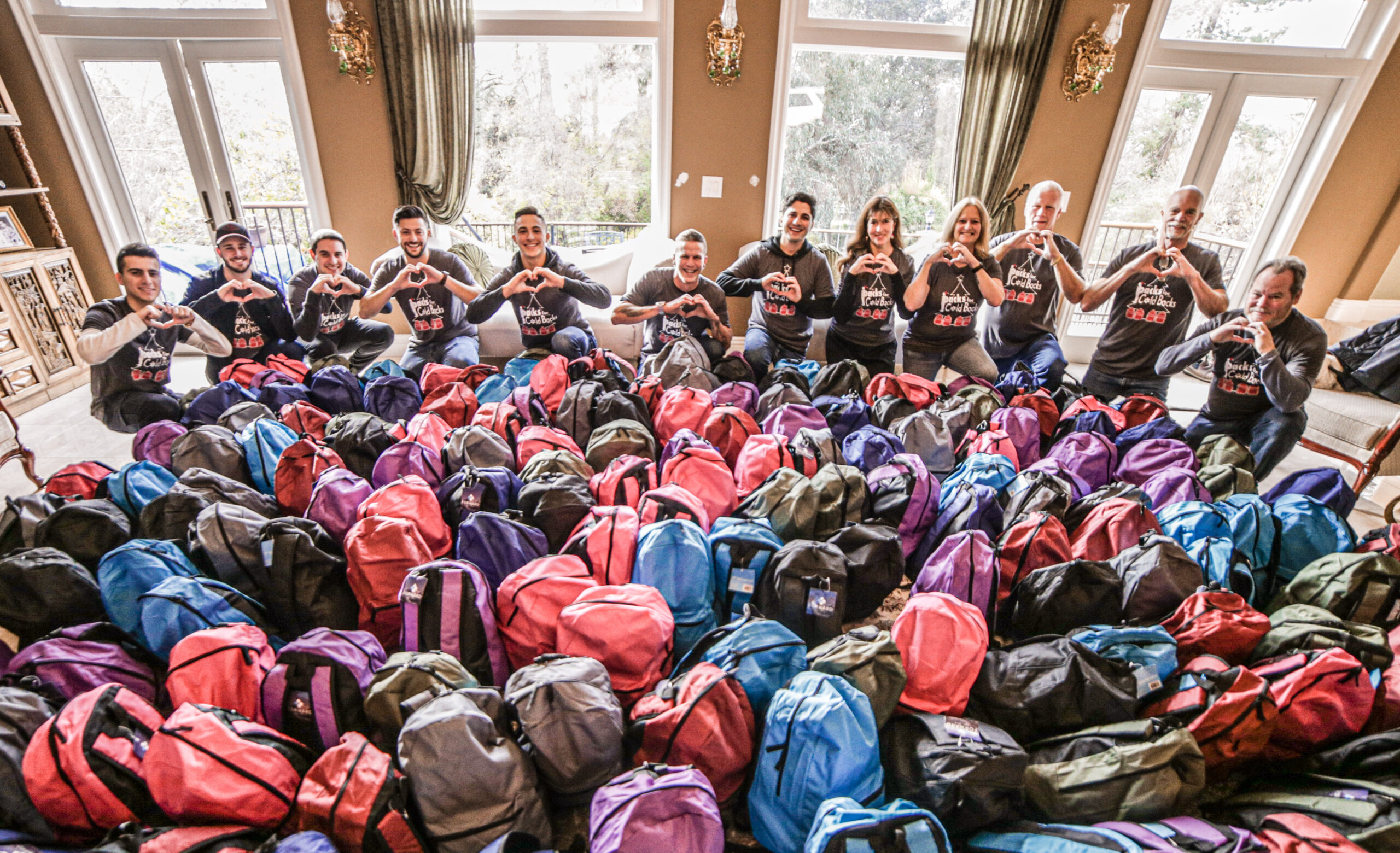 Packs for Cold Backs volunteers gathered behind rows of backpacks prepared for the organization's annual Christmas outreach event.